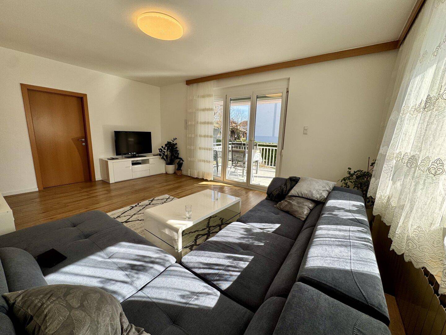 Gemütliches Wohnzimmer mit viel Tageslicht und Zugang zum Balkon, ideal zum Entspannen.