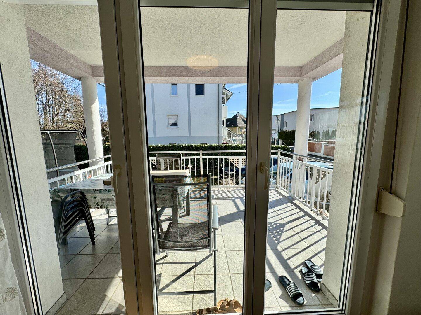 Blick vom Wohnzimmer auf den überdachten Balkon mit Fliesenboden und Sitzgelegenheiten.