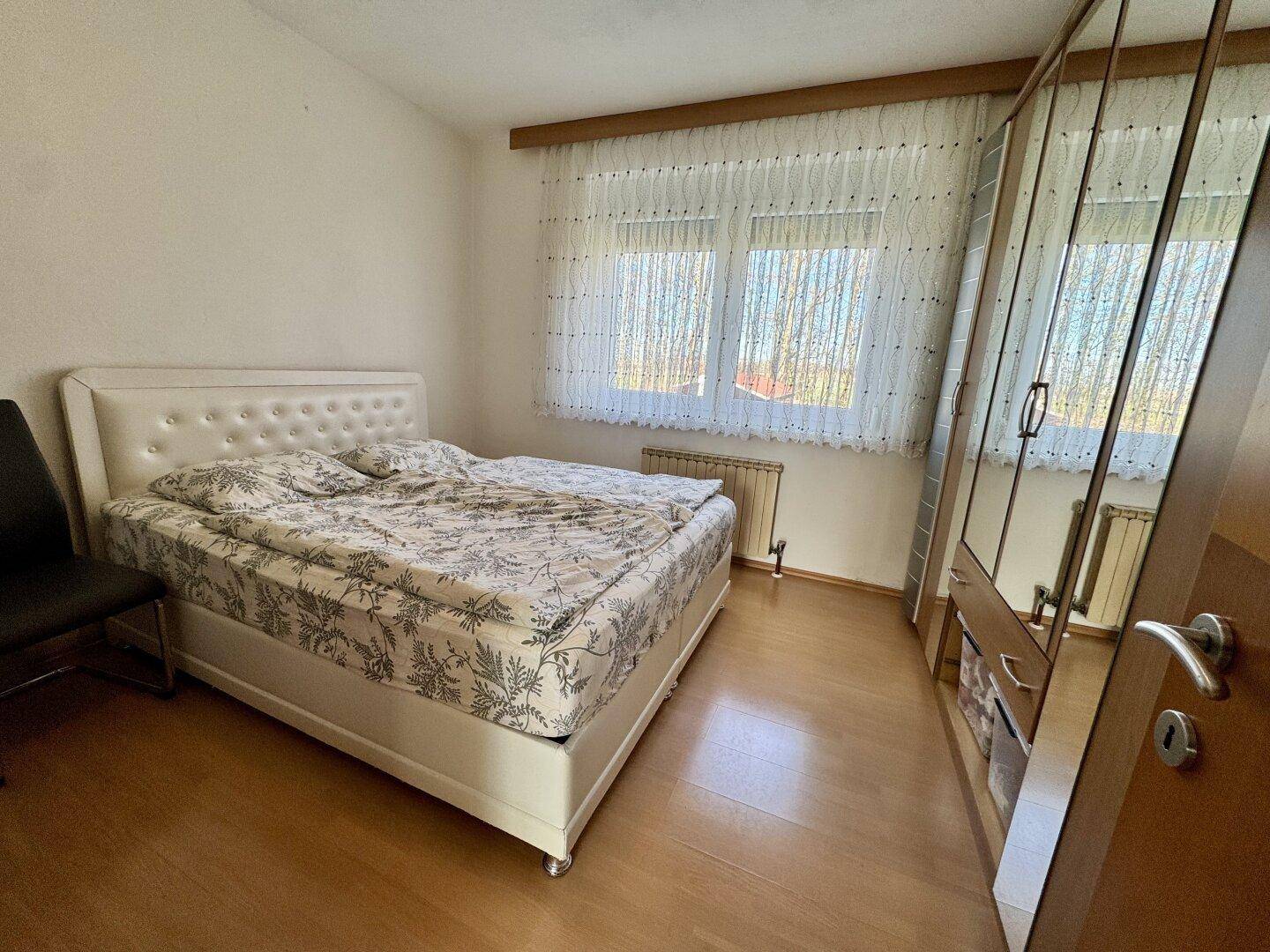 Schlafzimmer mit Doppelbett, großem Spiegelschrank und Laminatboden.