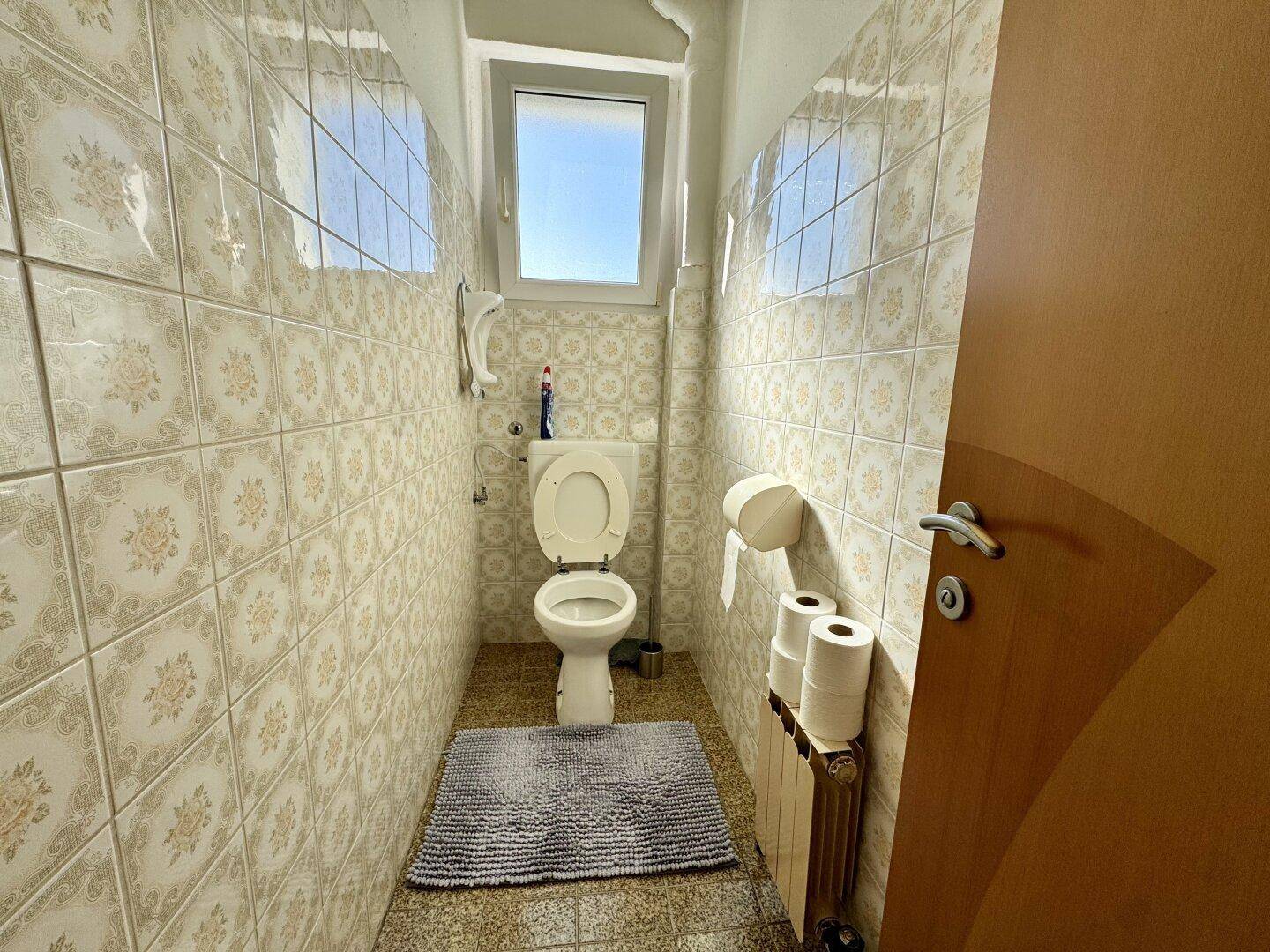 Separate Toilette mit Fenster und gemusterten Fliesen, funktional und hell.