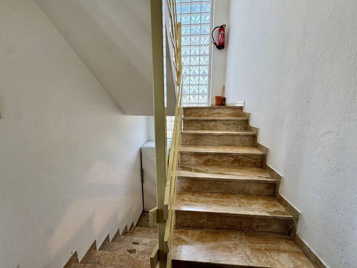 Treppenhaus mit Fliesenstufen und Glasbausteinwand für natürliches Licht.