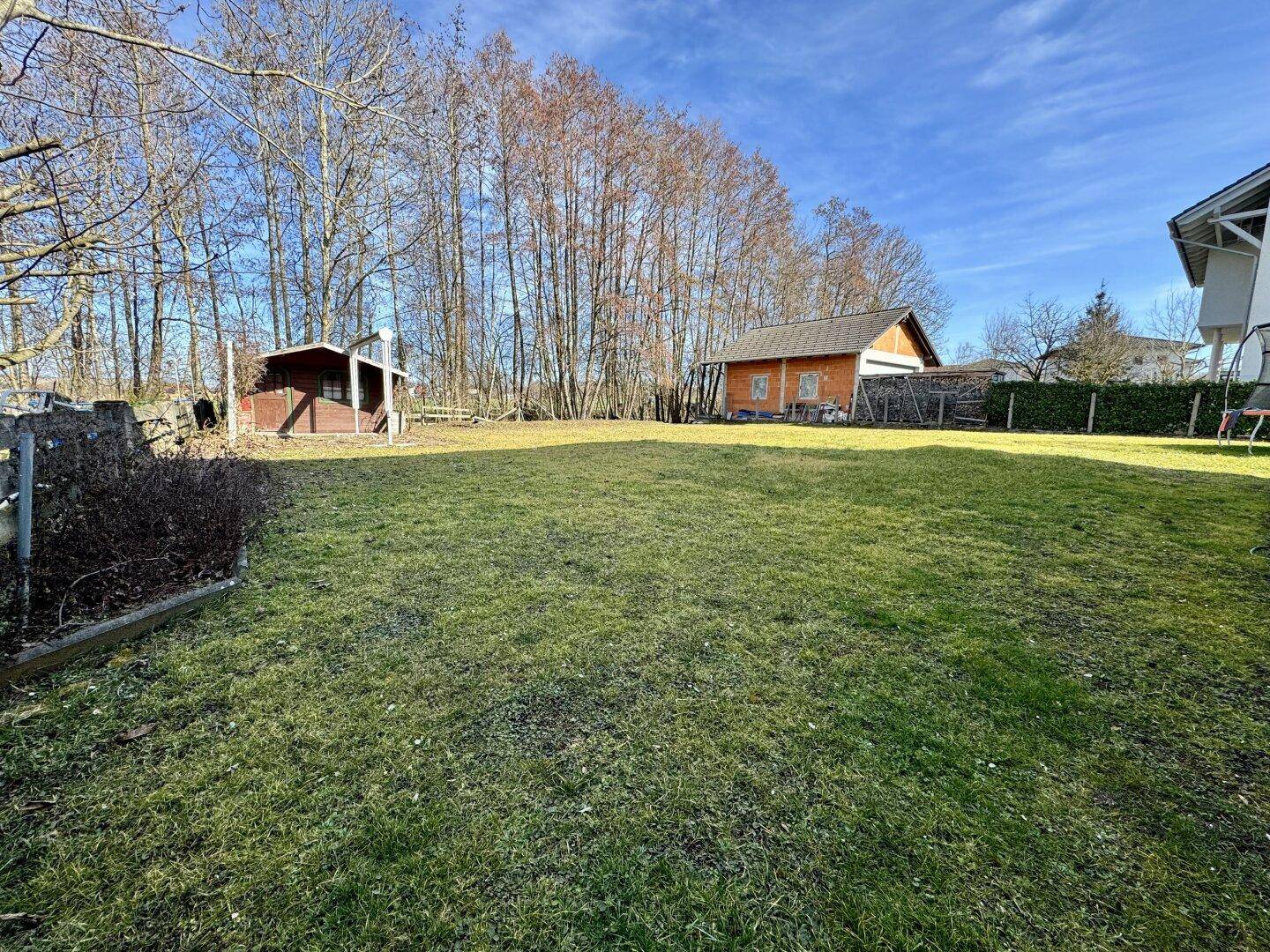 Großer, gepflegter Garten mit Rasenfläche und Gartenhäusern im Hintergrund.