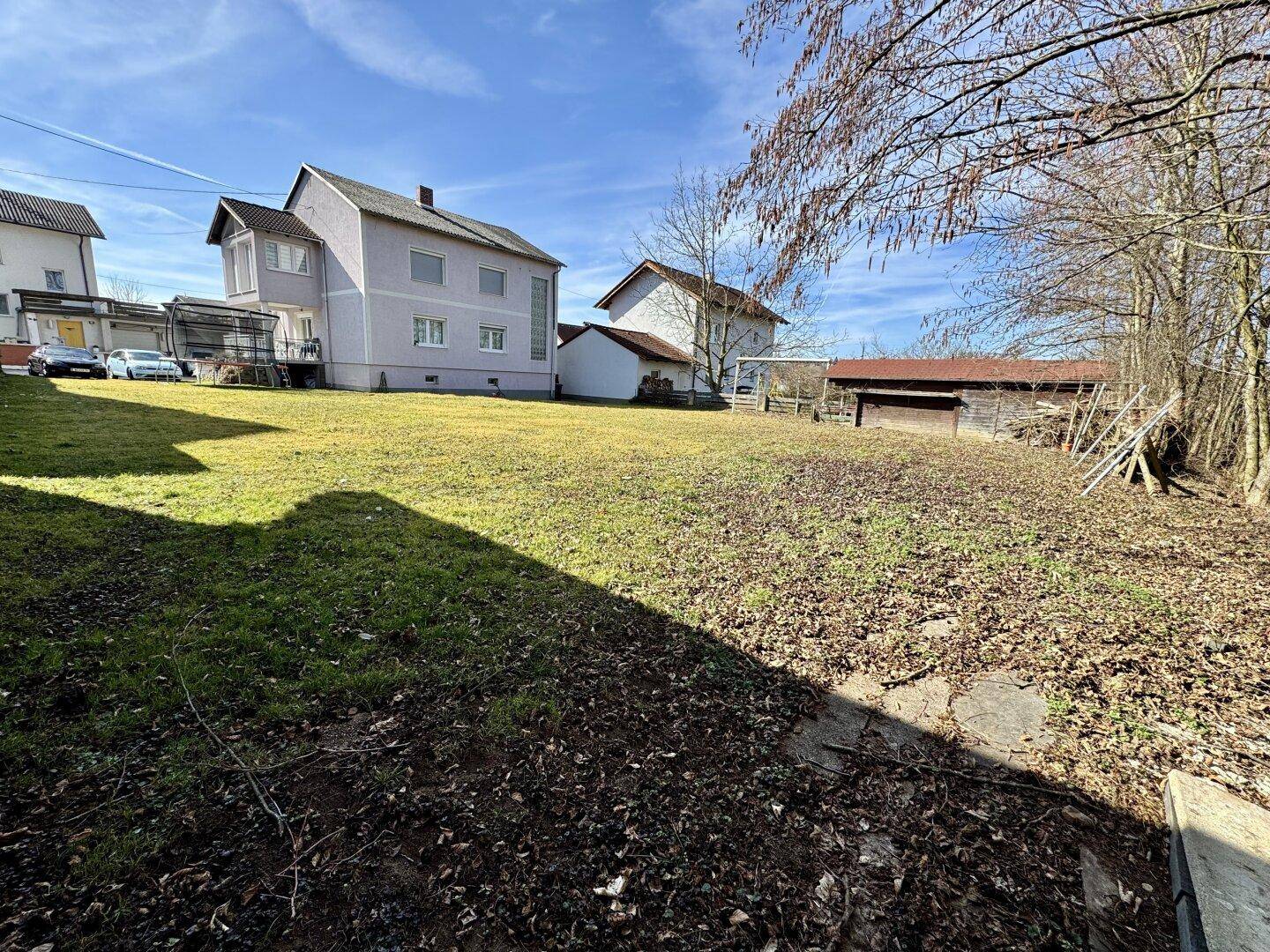 Großer, sonniger Gartenbereich mit Rasenfläche hinter dem Wohnhaus und Bäumen im Hintergrund.