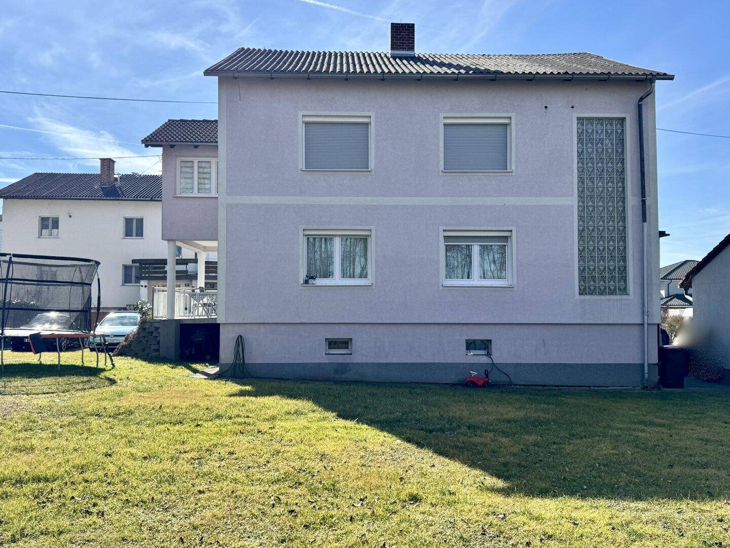 Rückseite des Hauses mit Garten, Rasenfläche und Trampolin unter blauem Himmel.