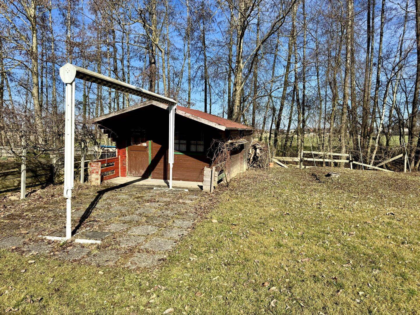 Rustikales Gartenhaus aus Holz am Rande des Grundstücks, umgeben von Grün.