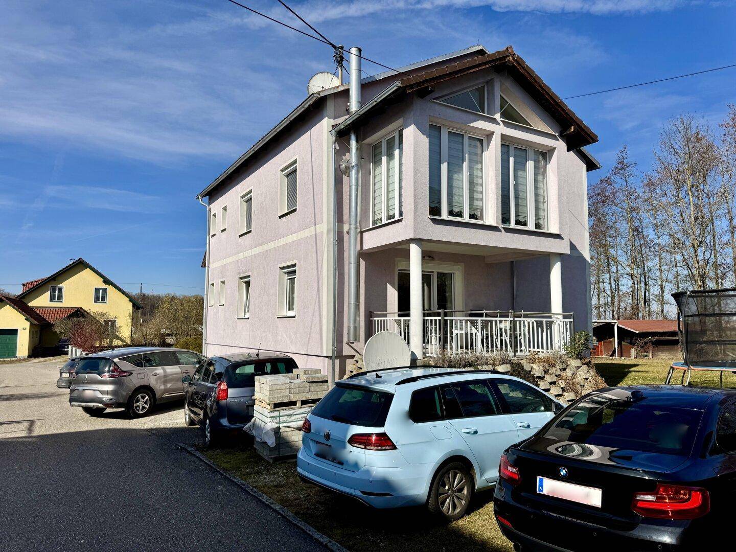 Vorderansicht des Hauses mit geparkten Autos auf dem Stellplatz an einem sonnigen Tag.