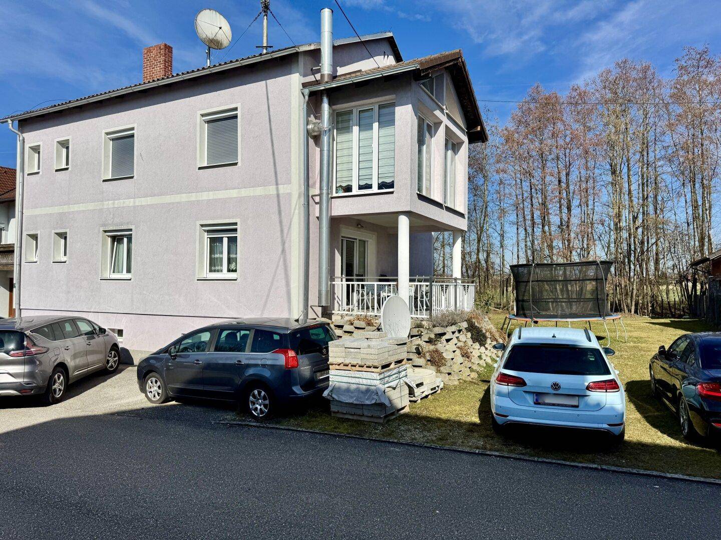 Seitenansicht des Hauses mit geparkten Fahrzeugen und angrenzendem Gartenbereich.
