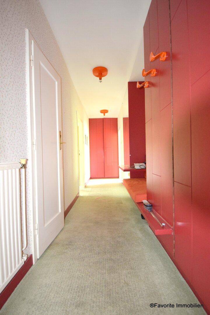 Langer Flur mit rotem Einbauschrank, Teppichboden und Deckenleuchten.