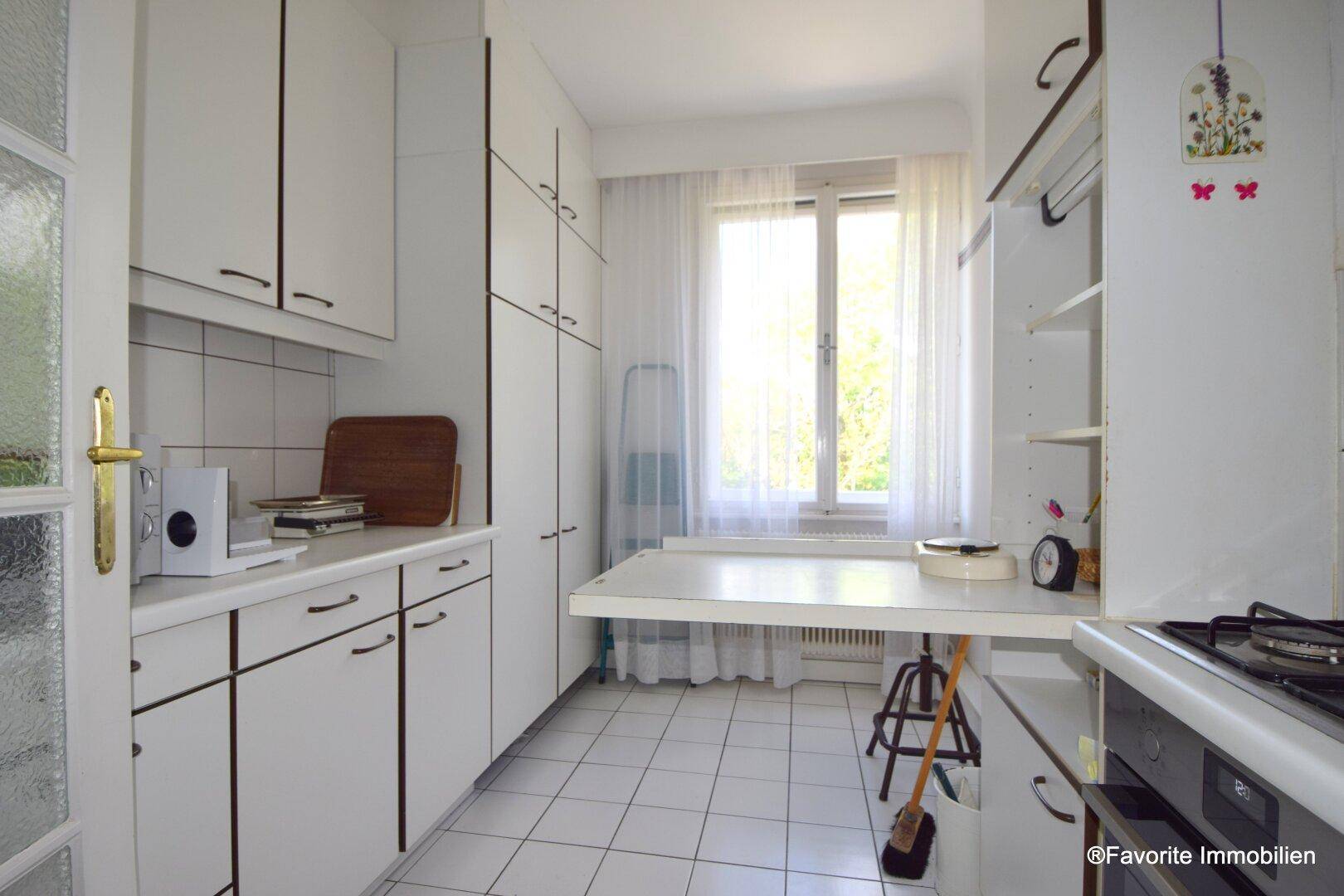 Funktionale Küche mit weißen Schränken, Fliesenboden und Fenster zum Außenbereich.