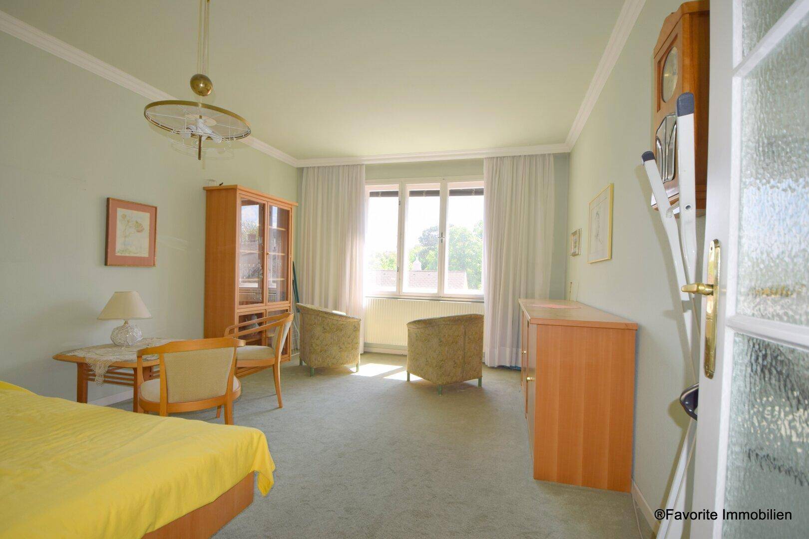 Helles Schlafzimmer mit Teppichboden, gelbem Bett und Blick ins Grüne durch große Fenster.