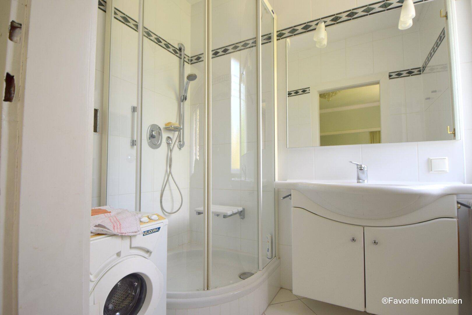 Badezimmer mit Duschkabine, Waschbecken und Waschmaschine.