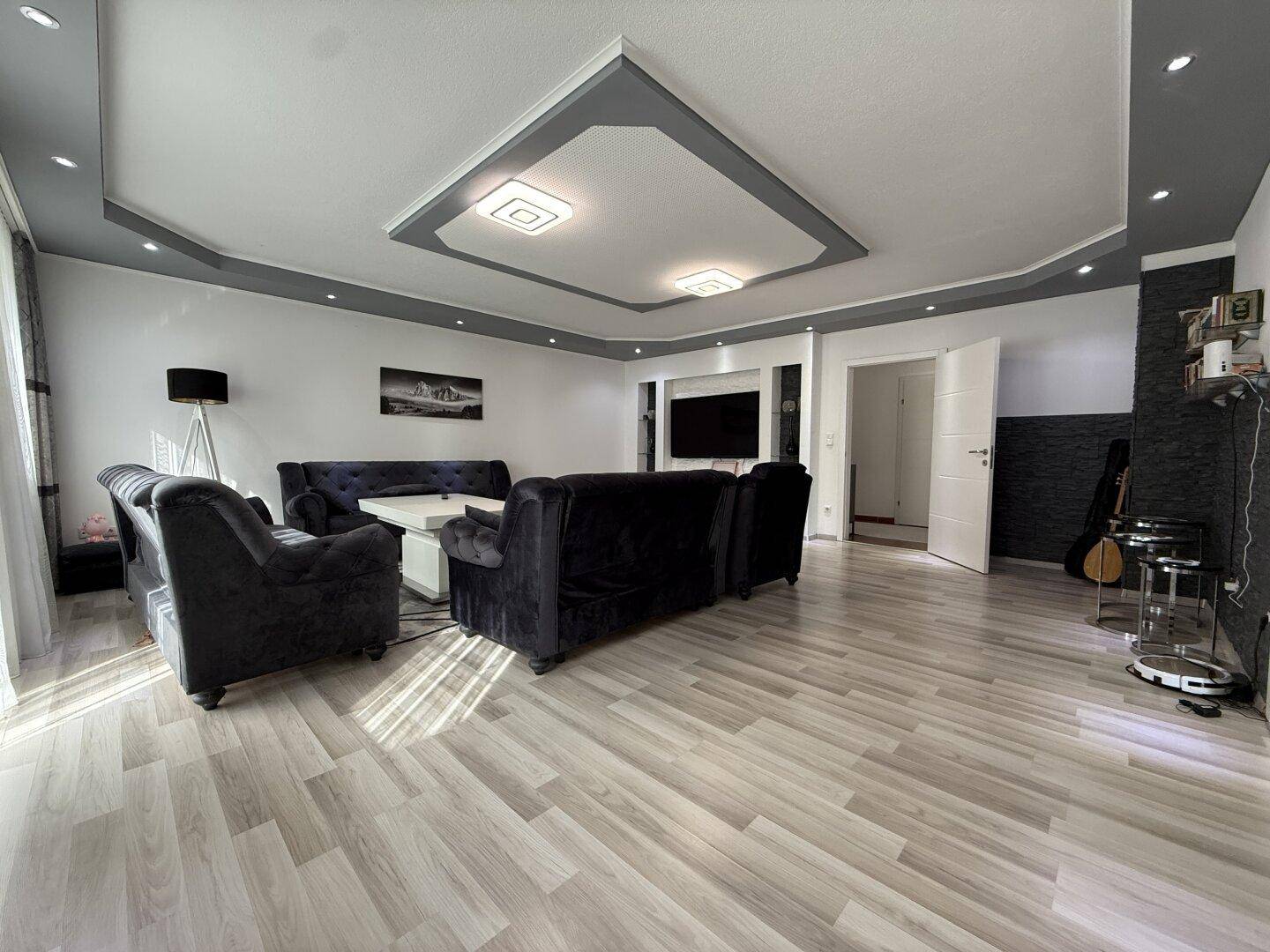 Helles Wohnzimmer mit dunklen Sitzmöbeln, Laminatboden und dekorativer Deckenbeleuchtung.