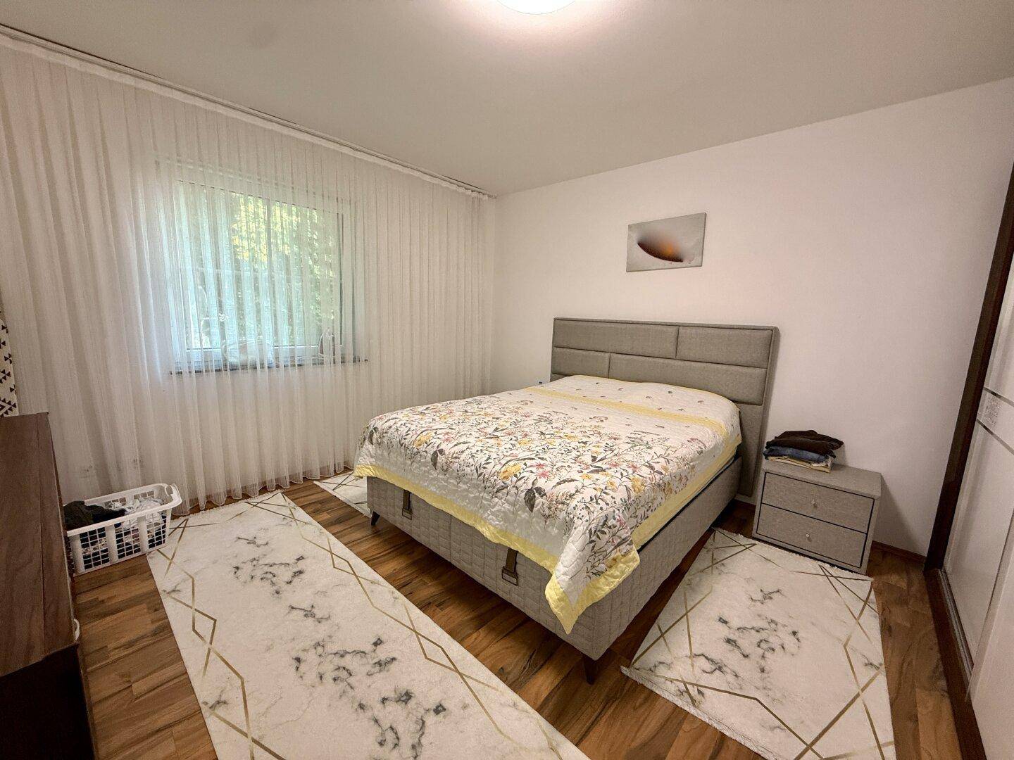 Gemütliches Schlafzimmer mit Doppelbett, Holzboden und großem Fenster mit Vorhängen.