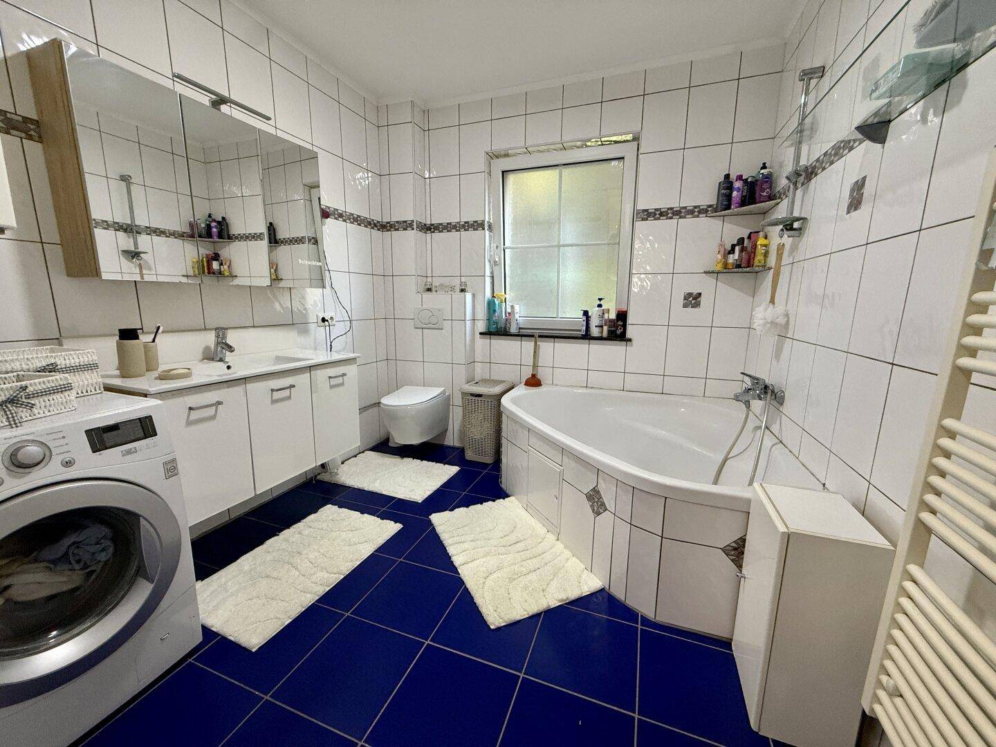 Geräumiges Badezimmer mit blauen Fliesen, Badewanne, Waschmaschine und Fenster.
