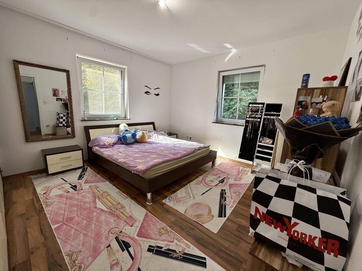 Helles Schlafzimmer mit Holzboden, Doppelbett und zwei Fenstern.