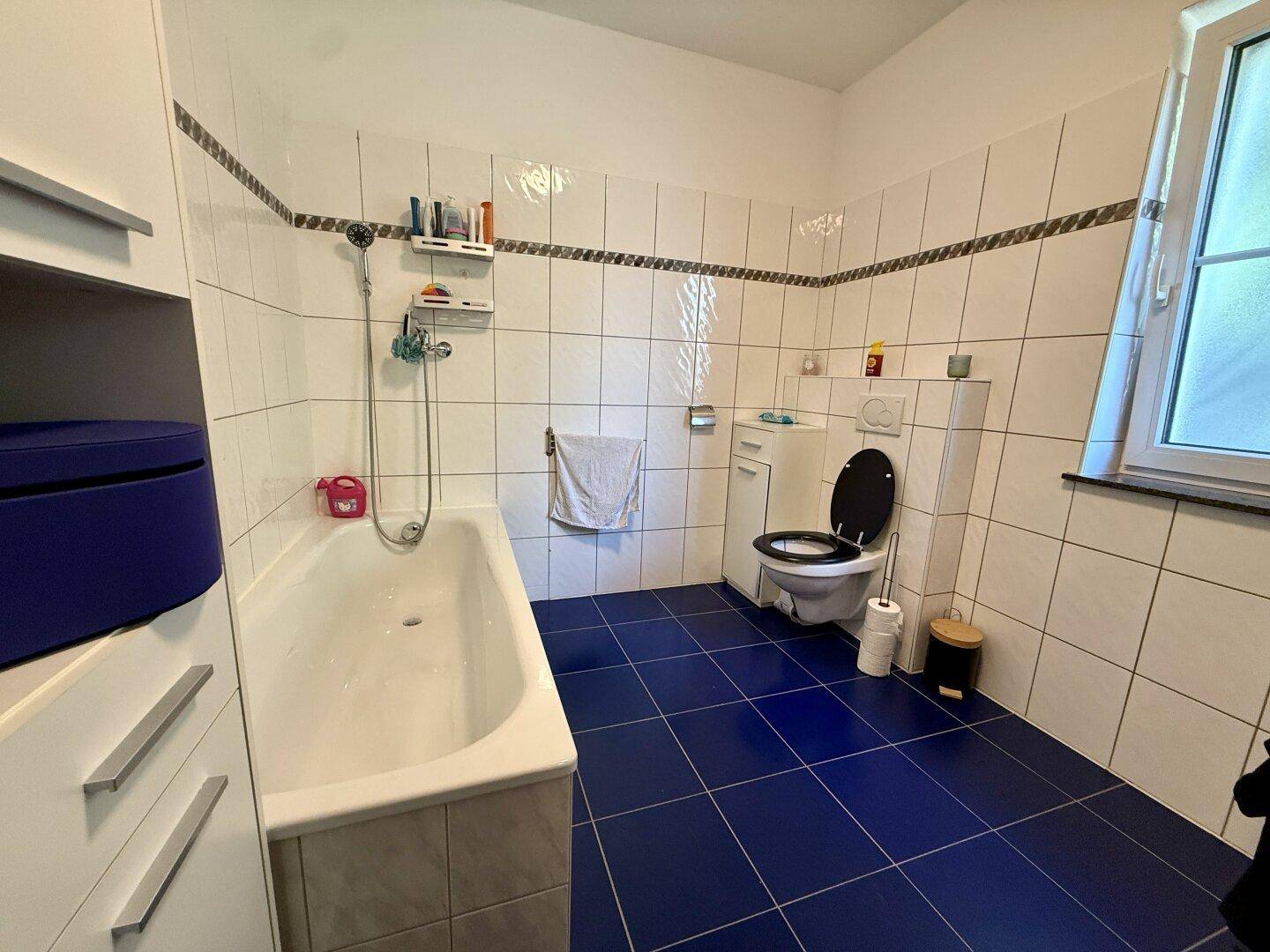 Kleines Badezimmer mit Badewanne, Toilette, blauen Fliesen und Fenster.