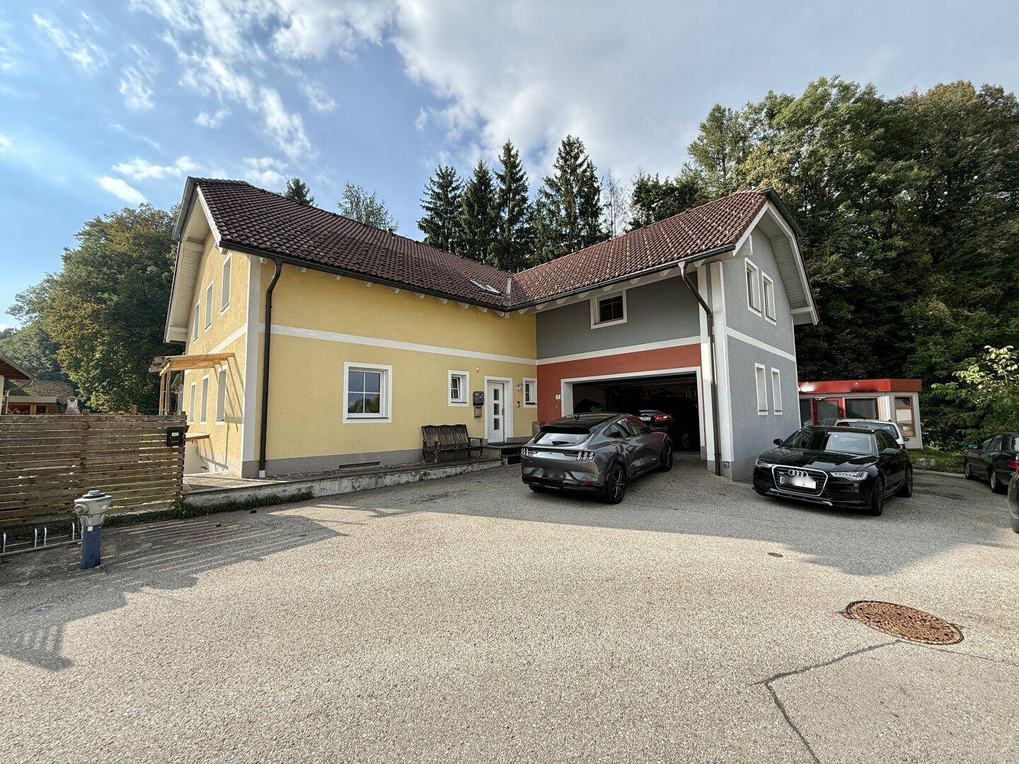 Mehrfamilienhaus mit gelber und grauer Fassade, Garagen und Stellplätzen.
