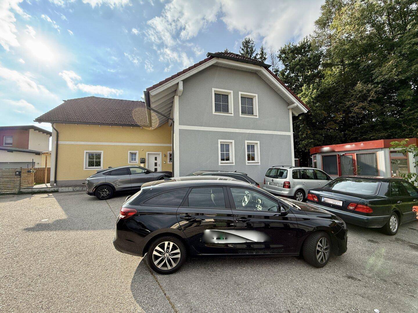 Ansicht des Hauses mit grauer und gelber Fassade und gepflastertem Vorplatz.