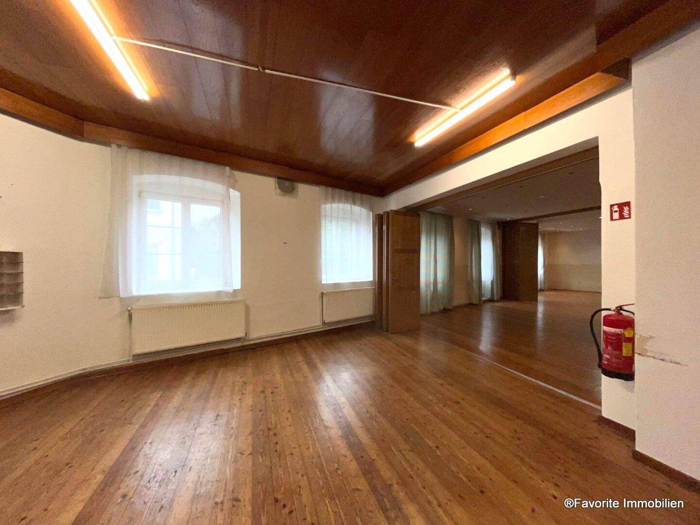 Geräumiger, leerer Saal mit Holzboden, hohen Decken und großen Fenstern, bereit für zukünftige Veranstaltungen.