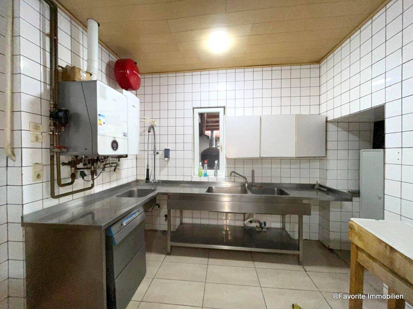 Funktionale Gewerbeküche mit Edelstahlspülen, weißen Fliesenwänden und Gastherme, bereit für den professionellen Betrieb.
