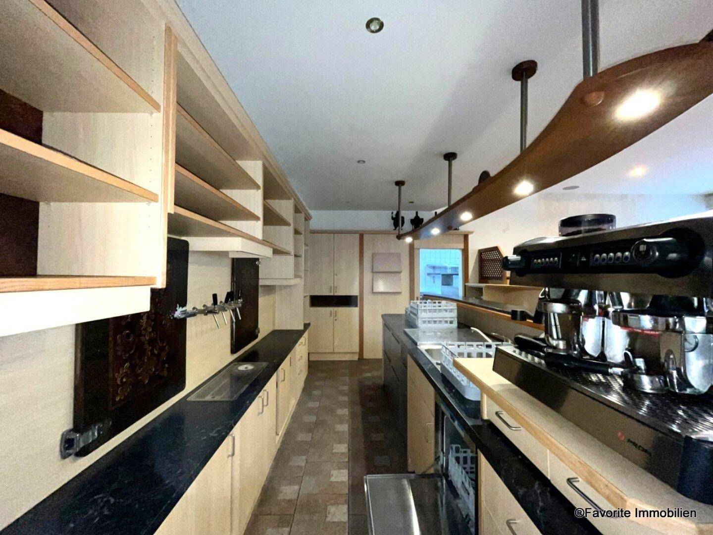 Langer Barbereich mit Holzregalen, dunkler Arbeitsplatte und professioneller Kaffeemaschine, gut ausgestattet für Gäste.