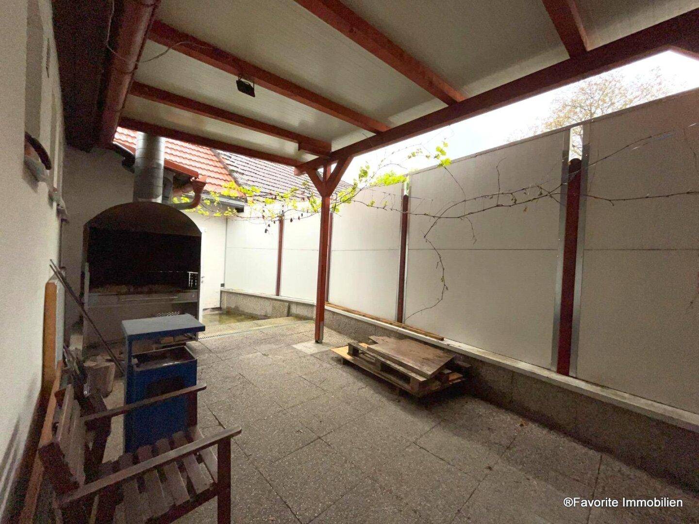 Überdachter Außenbereich mit festem Grill, gepflastertem Boden und Holzbänken, ideal für entspannte Sommerabende.
