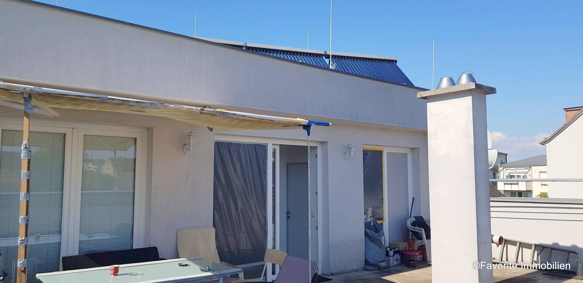Dachterrasse mit Sonnenschutz und Blick auf die Umgebung, mit sichtbaren Solarpaneelen auf dem Dach.