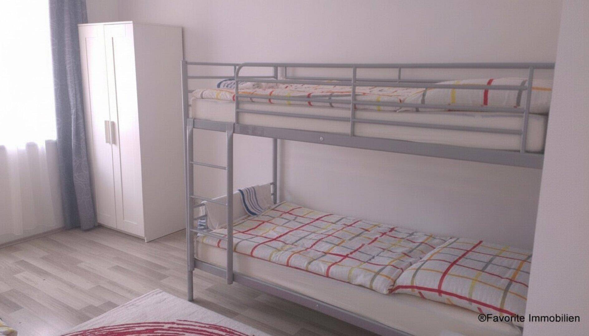 Helles Schlafzimmer mit Etagenbett und Kleiderschrank, ausgestattet mit Laminatboden.