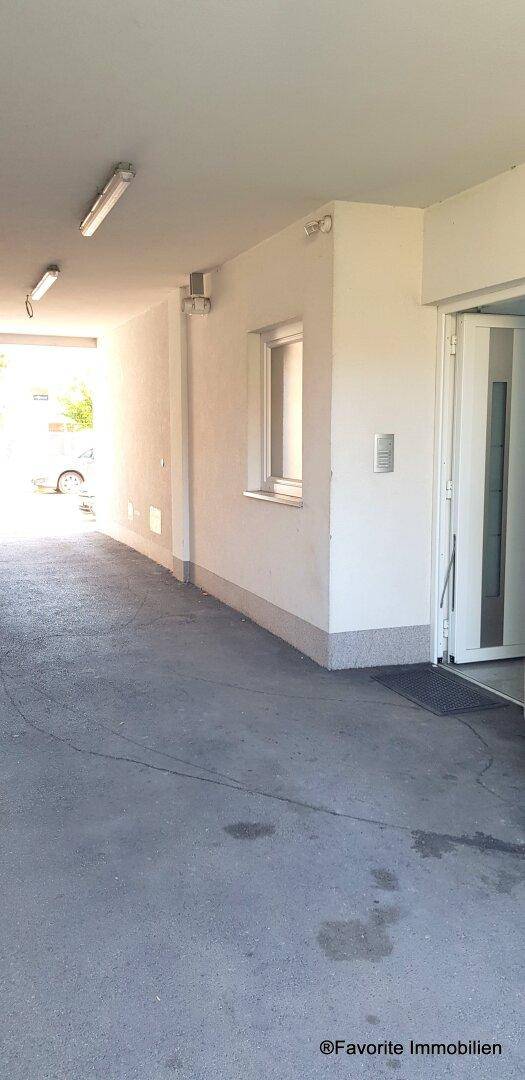 Überdachte Einfahrt oder Durchgang mit Betonboden und Beleuchtung, die zu einem Parkbereich führt.
