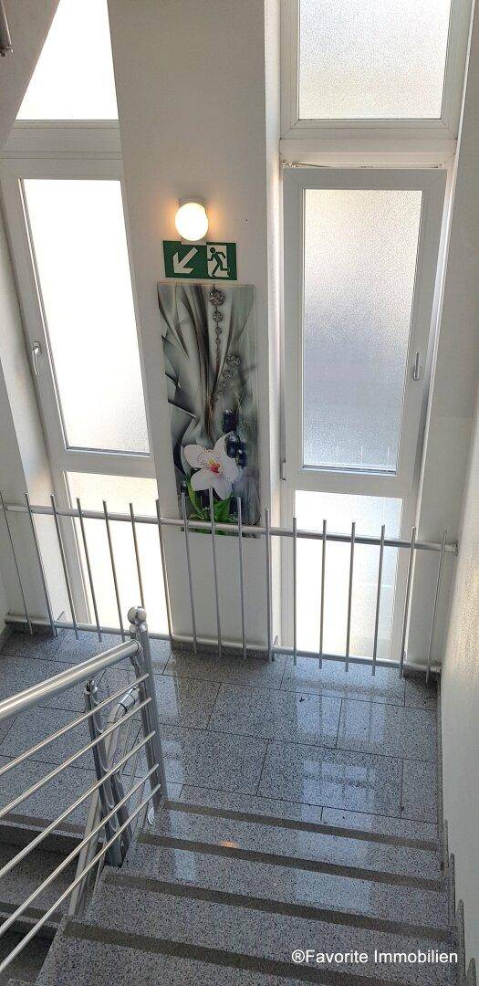 Treppenaufgang mit großen Fenstern und einem dekorativen Bild, das für Helligkeit sorgt.