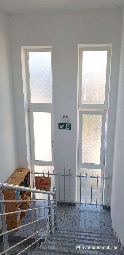 Heller Treppenaufgang mit großen Fenstern und Fliesenboden, der viel Tageslicht hereinlässt.