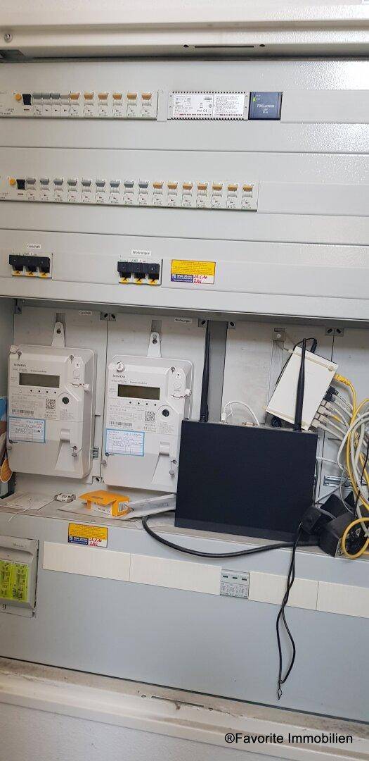 Elektrische Verteilung mit Zählern, Sicherungen und Netzwerkkomponenten in einem Technikraum.