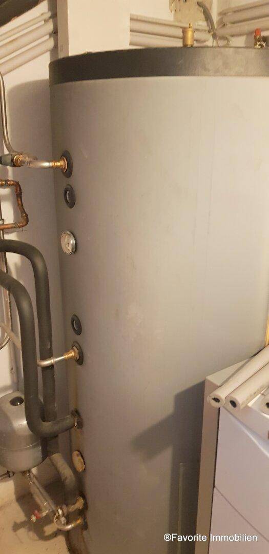 Großer Warmwasserspeicher in einem Technikraum, umgeben von Isolierungen und Rohren.