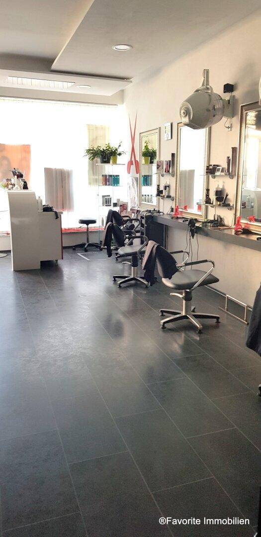 Geräumiger Friseursalon mit mehreren Arbeitsplätzen, dunklem Fliesenboden und großen Fenstern.