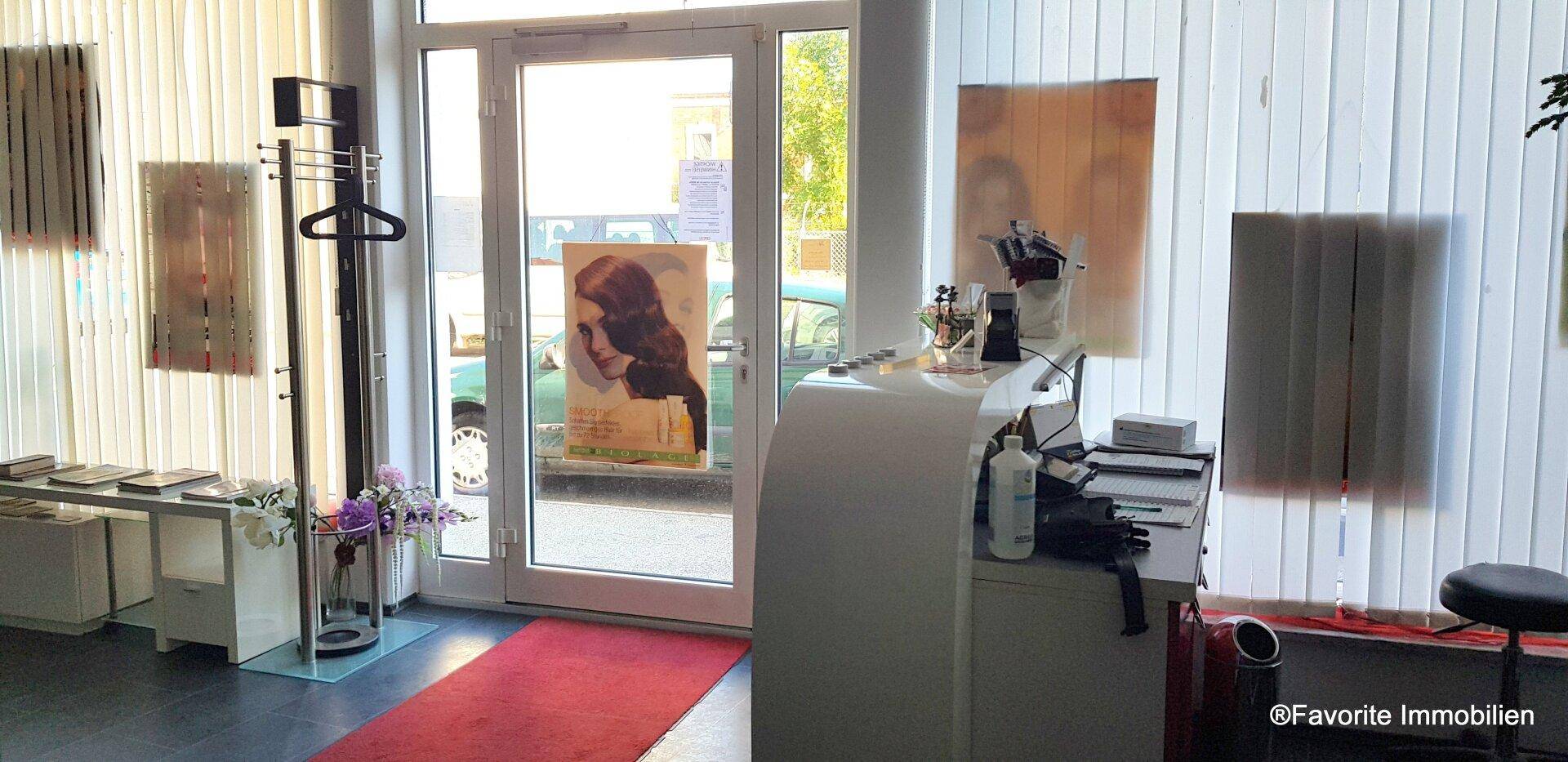 Eingangsbereich eines Geschäfts mit Schaufenstern, rotem Teppich und Blick zur Straße.