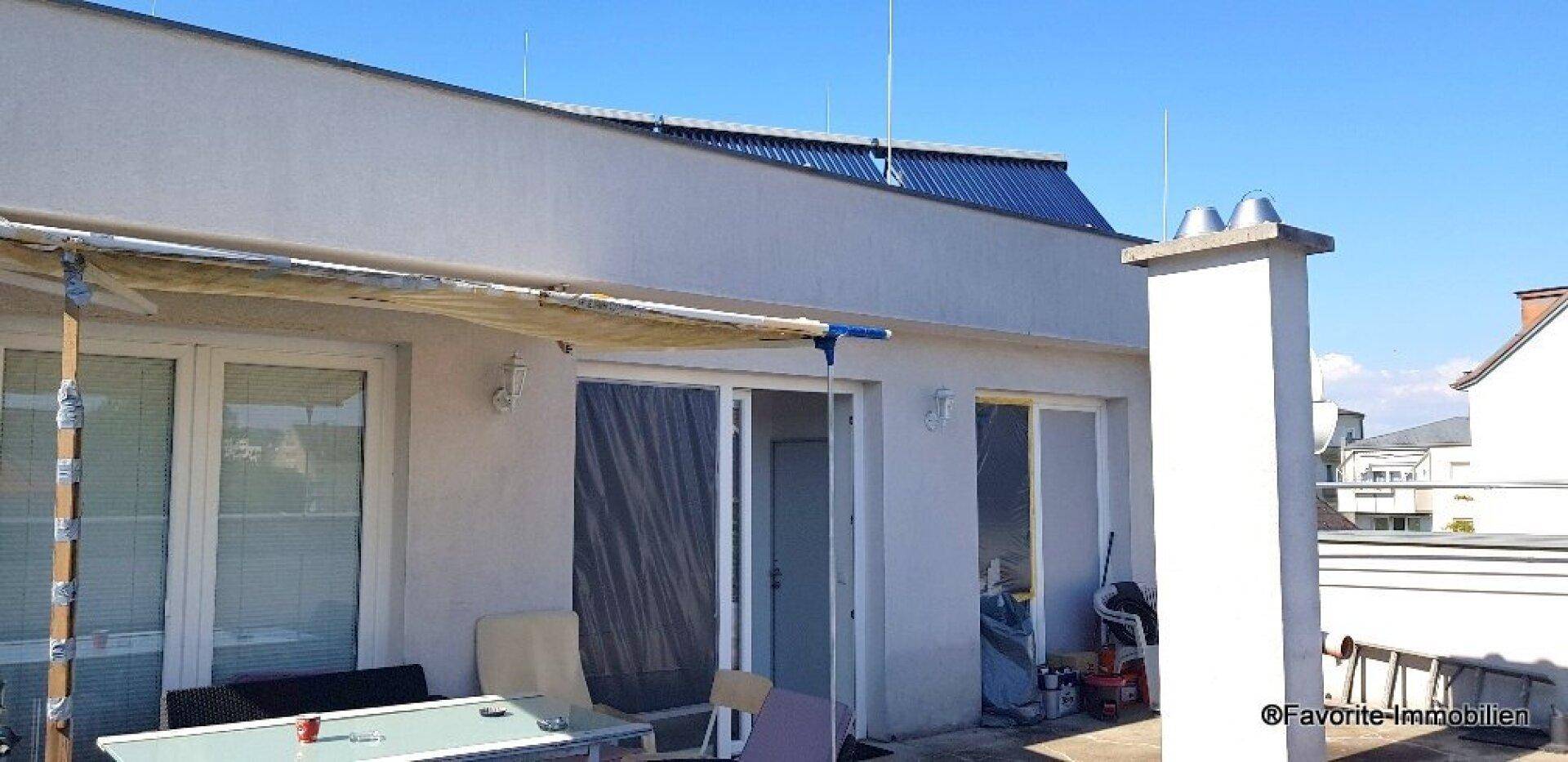 Dachterrasse mit Sonnenschutz und Blick auf die Umgebung, mit sichtbaren Solarpaneelen auf dem Dach.
