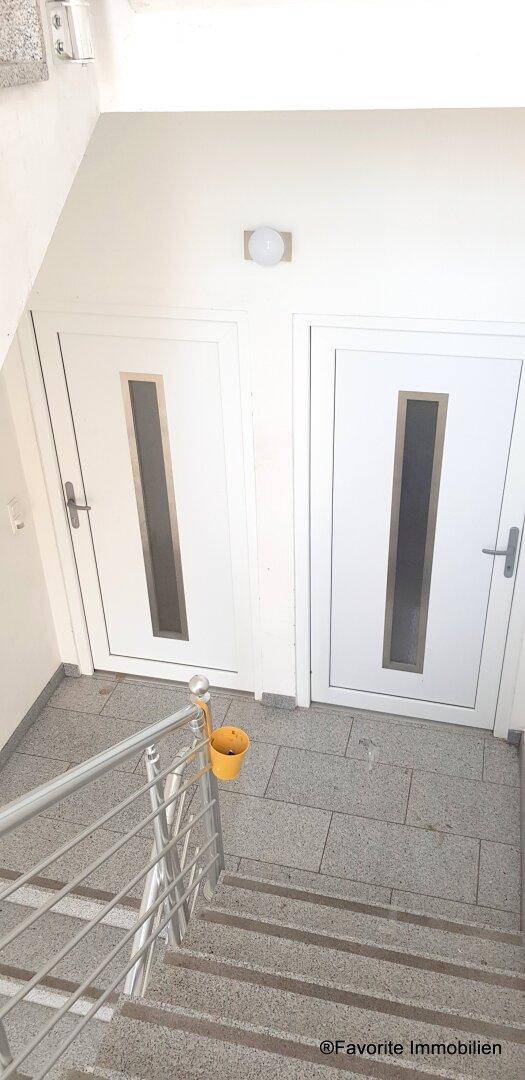 Treppenhaus mit Zugangstüren zu den Wohnungen und Fliesenboden, mit einem Eimer am Geländer.