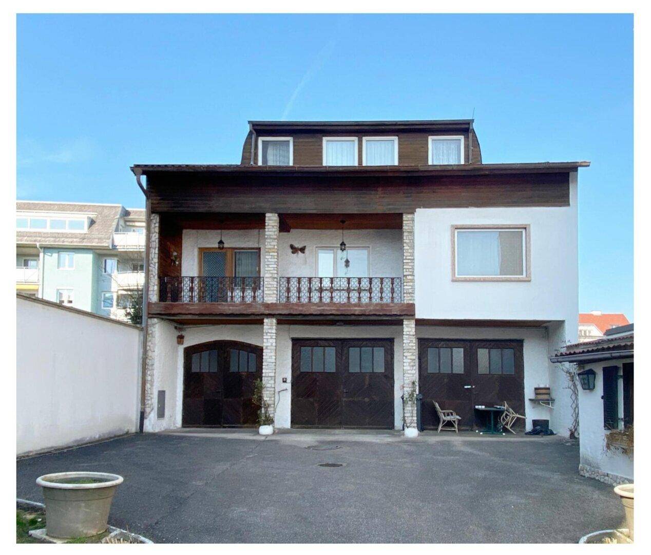 Rückansicht eines Hauses mit drei Garagen und einem Balkon im Obergeschoss.