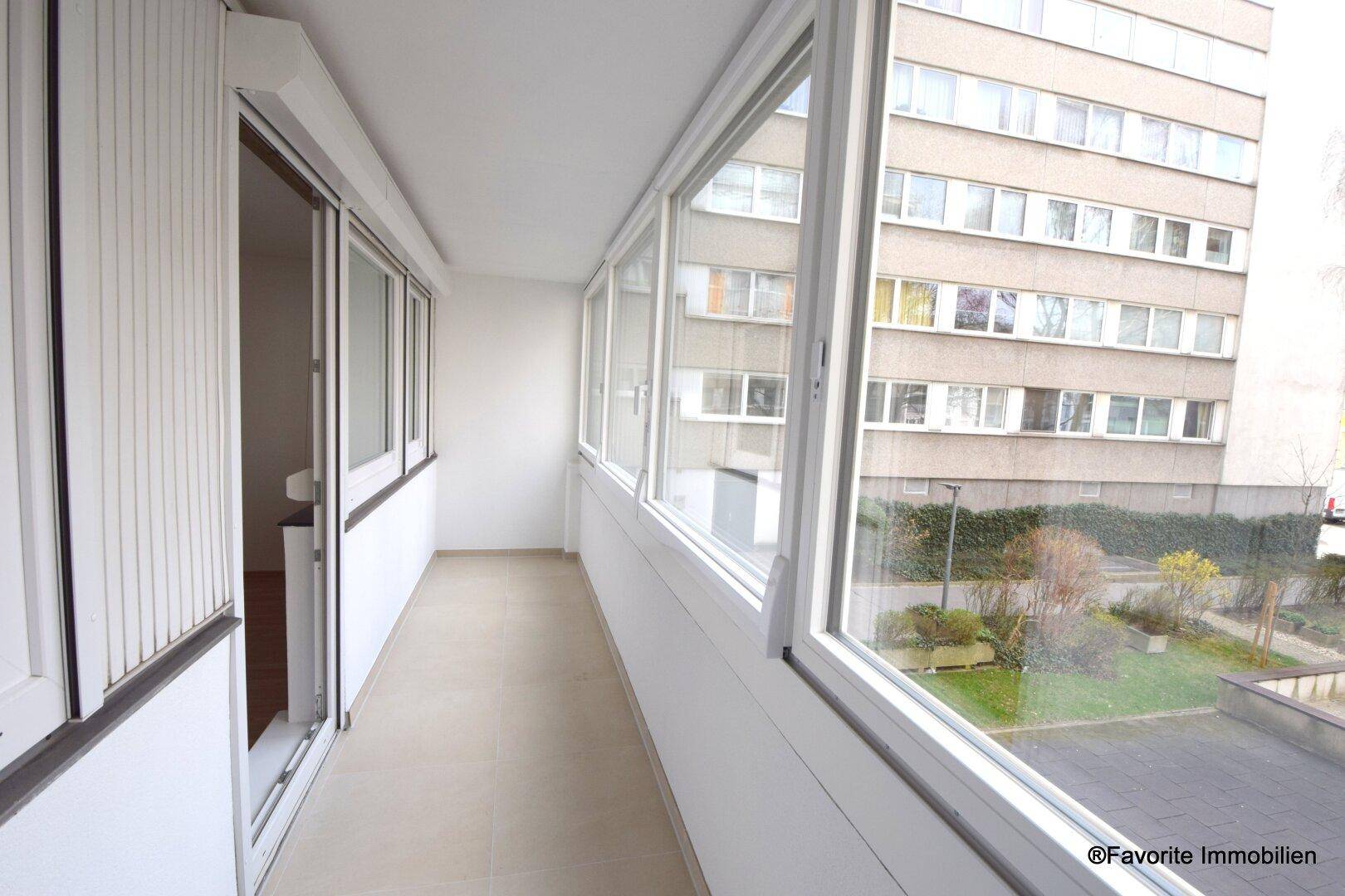 Helle, verglaste Loggia mit weitem Blick auf die Wohnanlage und die gepflegten Außenbereiche.