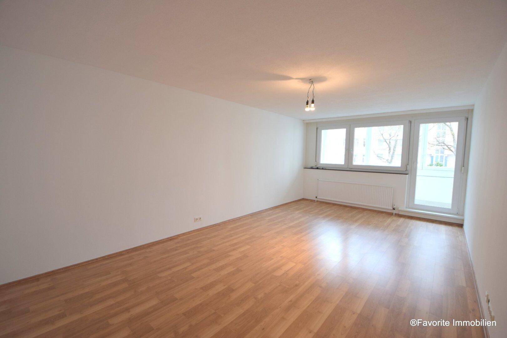 Geräumiges Wohnzimmer mit hellem Laminatboden und Zugang zu einem Balkon oder einer Loggia.