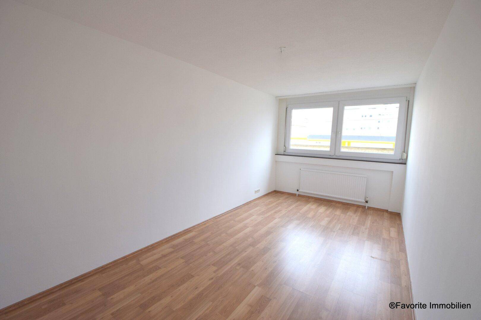 Helles Schlafzimmer mit Laminatboden und einem großen Fenster, das viel Tageslicht hereinlässt.