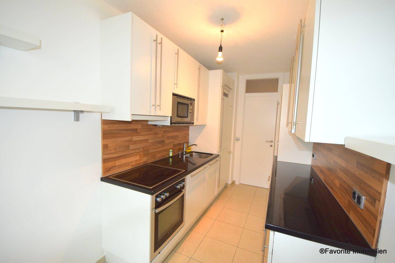 Moderne Einbauküche mit weißen Fronten, Holzrückwand und integrierten Geräten für effizientes Kochen.