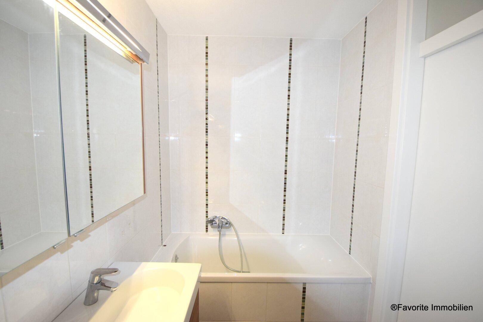 Helles Badezimmer mit Badewanne, weißen Fliesen und einem Spiegelschrank für zusätzlichen Stauraum.