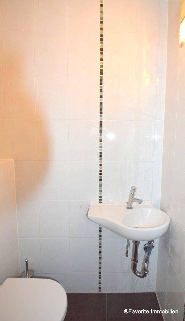 Separates WC mit wandhängender Toilette und kleinem Handwaschbecken, modern gefliest.