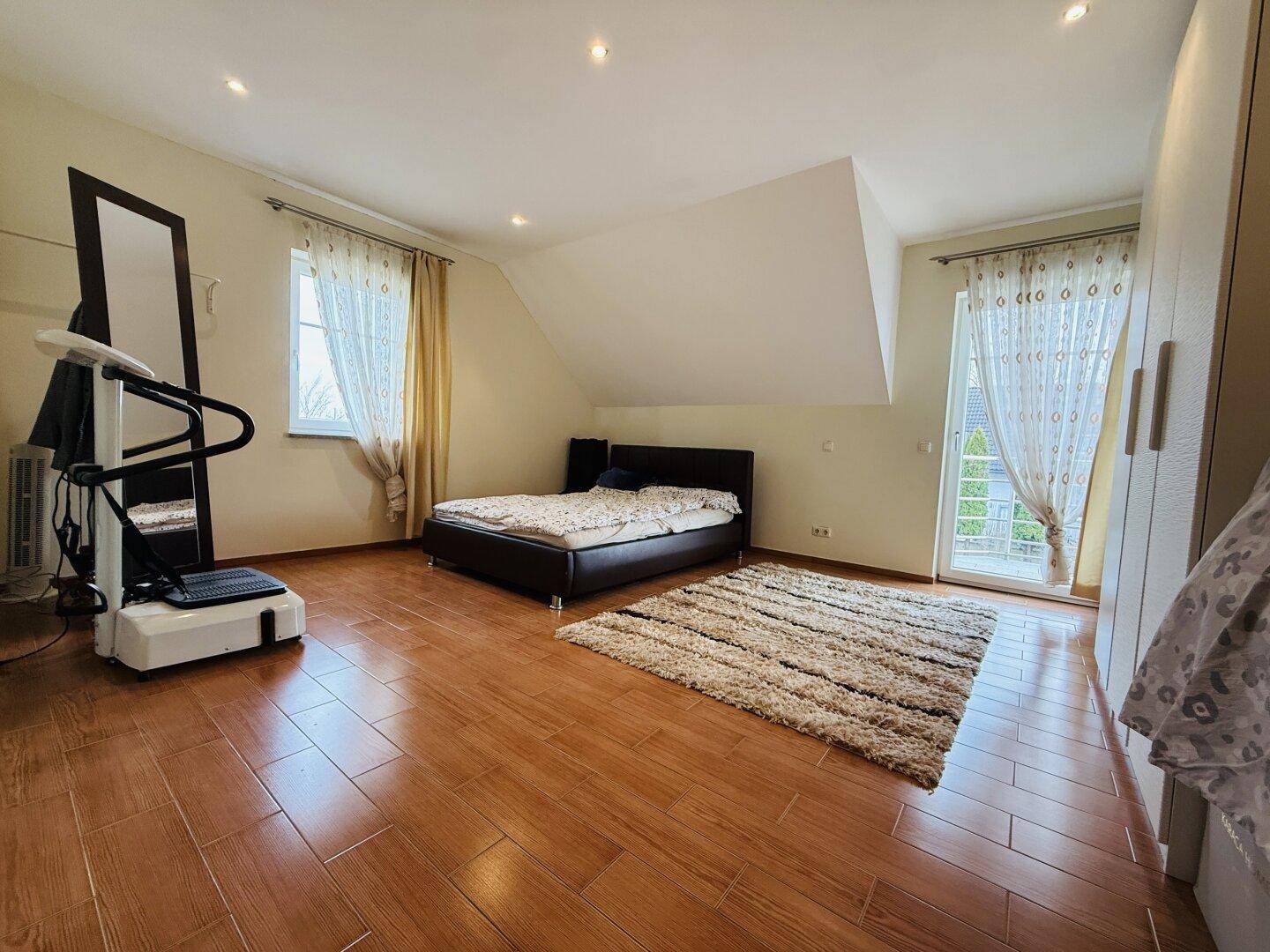 Geräumiges Schlafzimmer mit Holzboden, Doppelbett und Zugang zu einem französischen Balkon.
