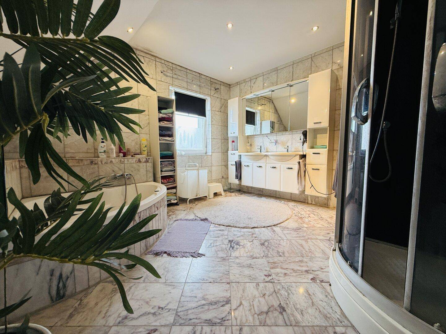 Großes Badezimmer mit Marmorfliesen, Eckbadewanne und separater Duschkabine, hell und geräumig.