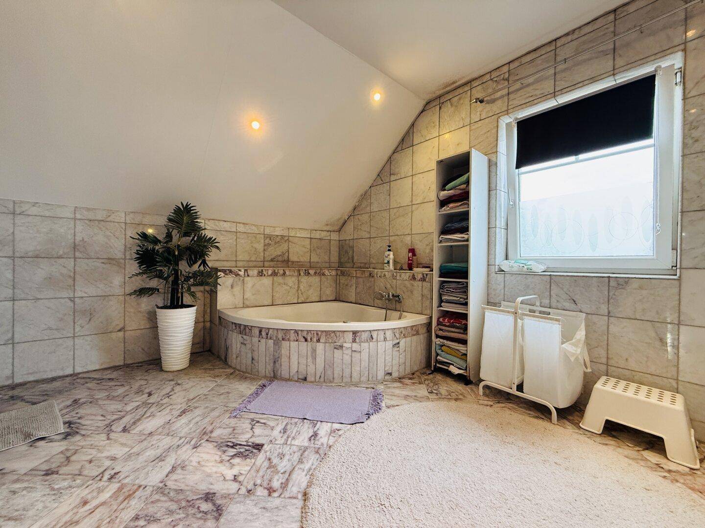 Helles Badezimmer mit Marmorfliesen, großer Eckbadewanne und Fenster für natürliches Licht.