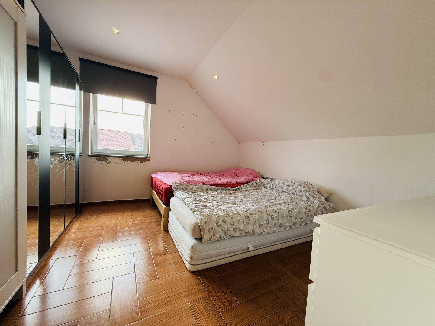 Gemütliches Schlafzimmer mit Holzboden, zwei Betten und Dachschräge, ideal für Kinder oder Gäste.