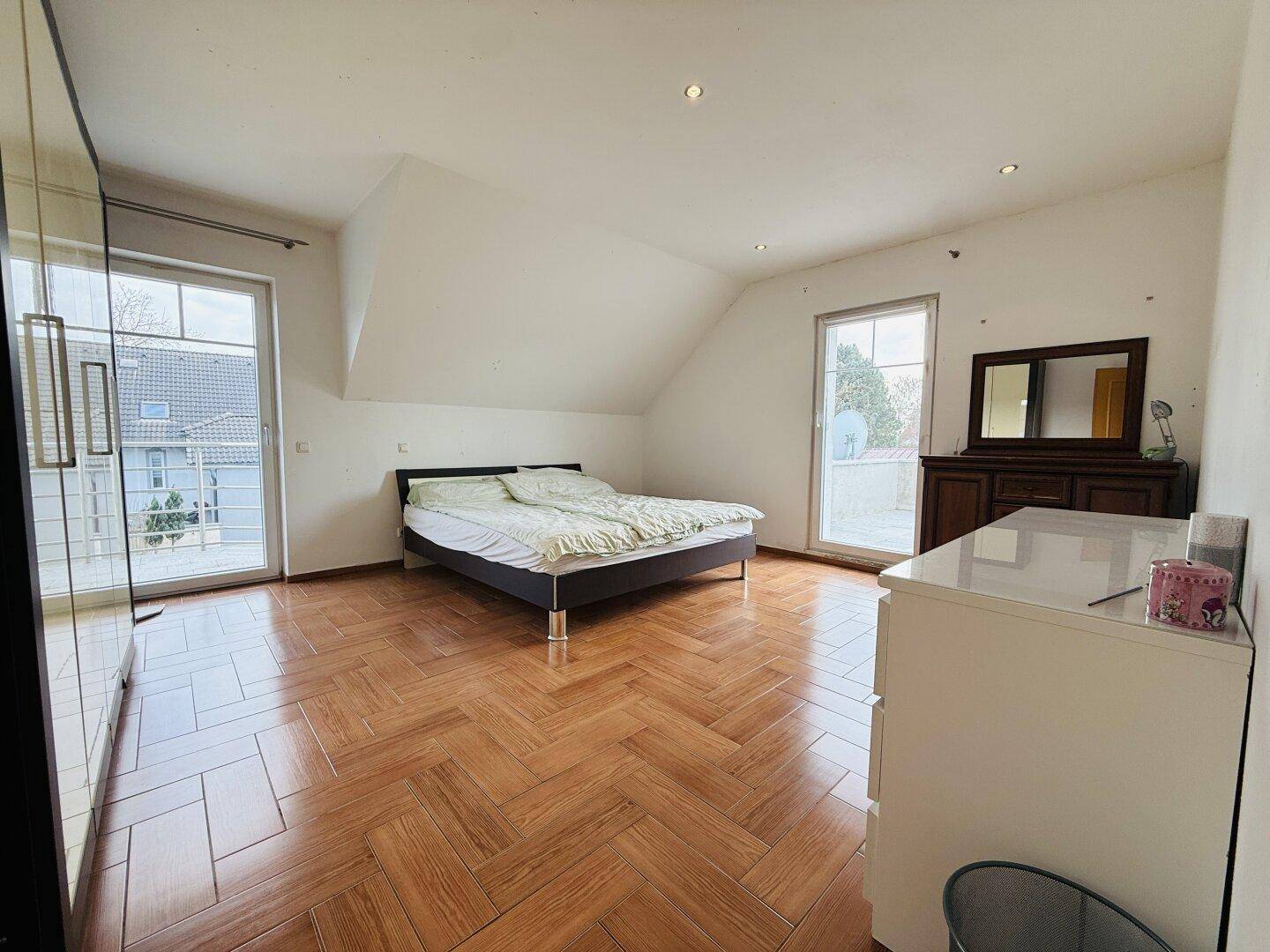 Helles Schlafzimmer mit Holzboden, Doppelbett und großen Fenstern, die viel Licht hereinlassen.
