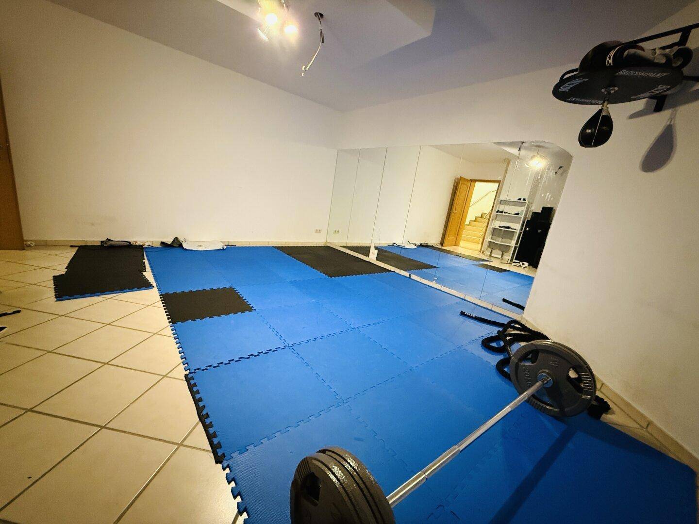 Fitnessraum im Untergeschoss mit blauen Matten und Hanteln, ideal für das Heimtraining.
